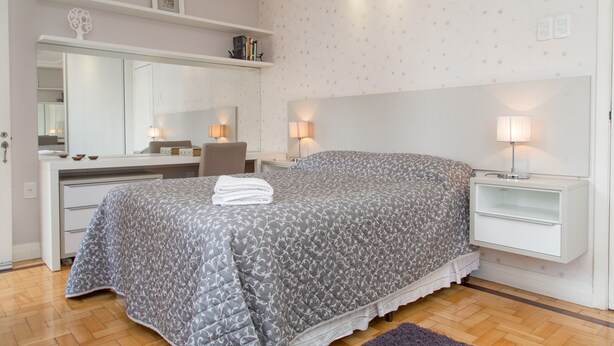 Un dormitorio con cama, mesitas de noche, cómoda, espejo y un papel tapiz con diseño.