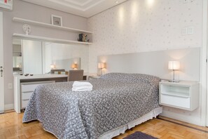 A bedroom with a bed, bedside tables, a dresser, a mirror, and a wall with a patterned wallpaper. - Apartamento Redenção (Porto Alegre)