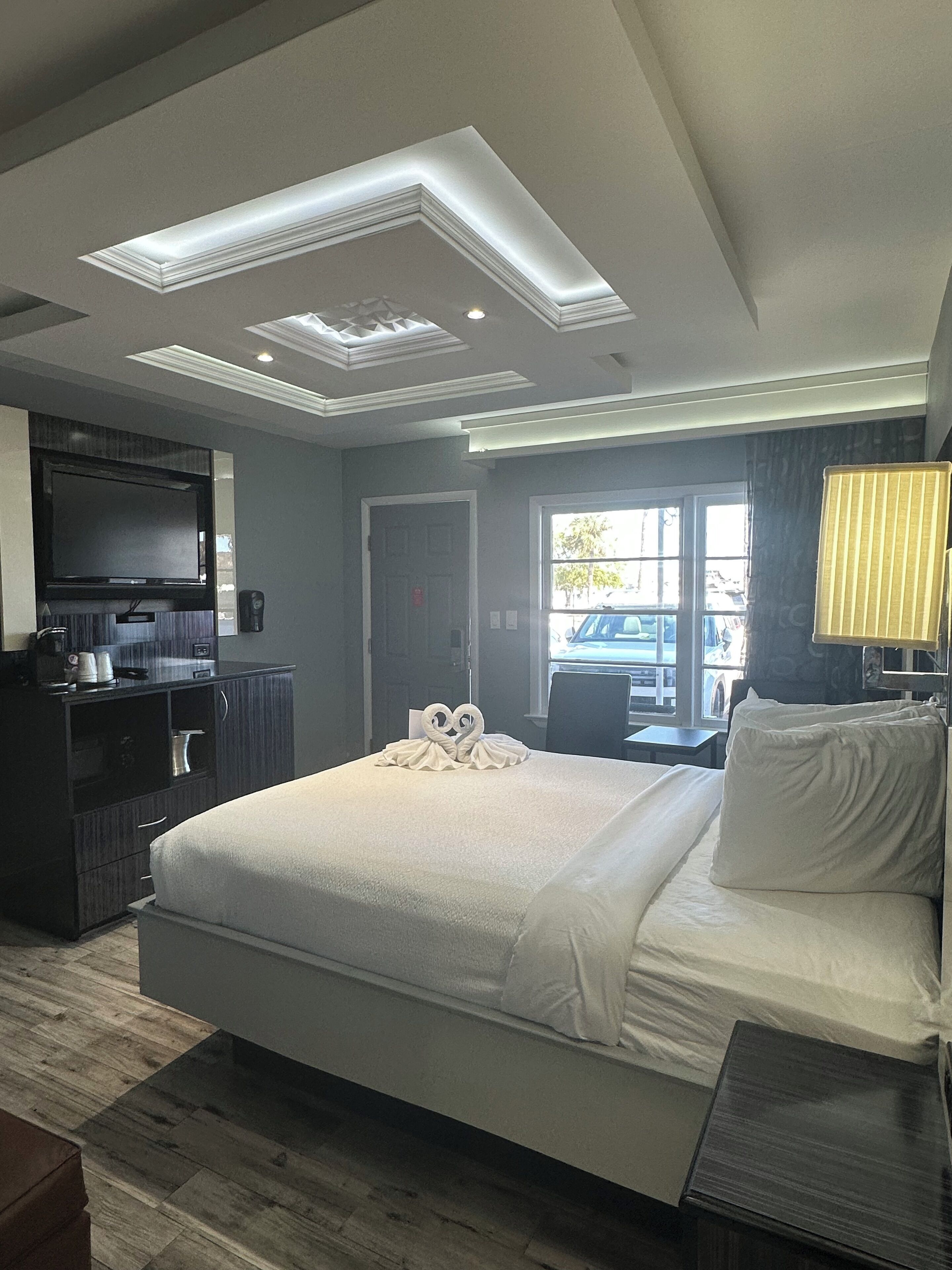 A hotel room with a large bed, a flat-screen TV, a minibar, and a window with a view of the outside.