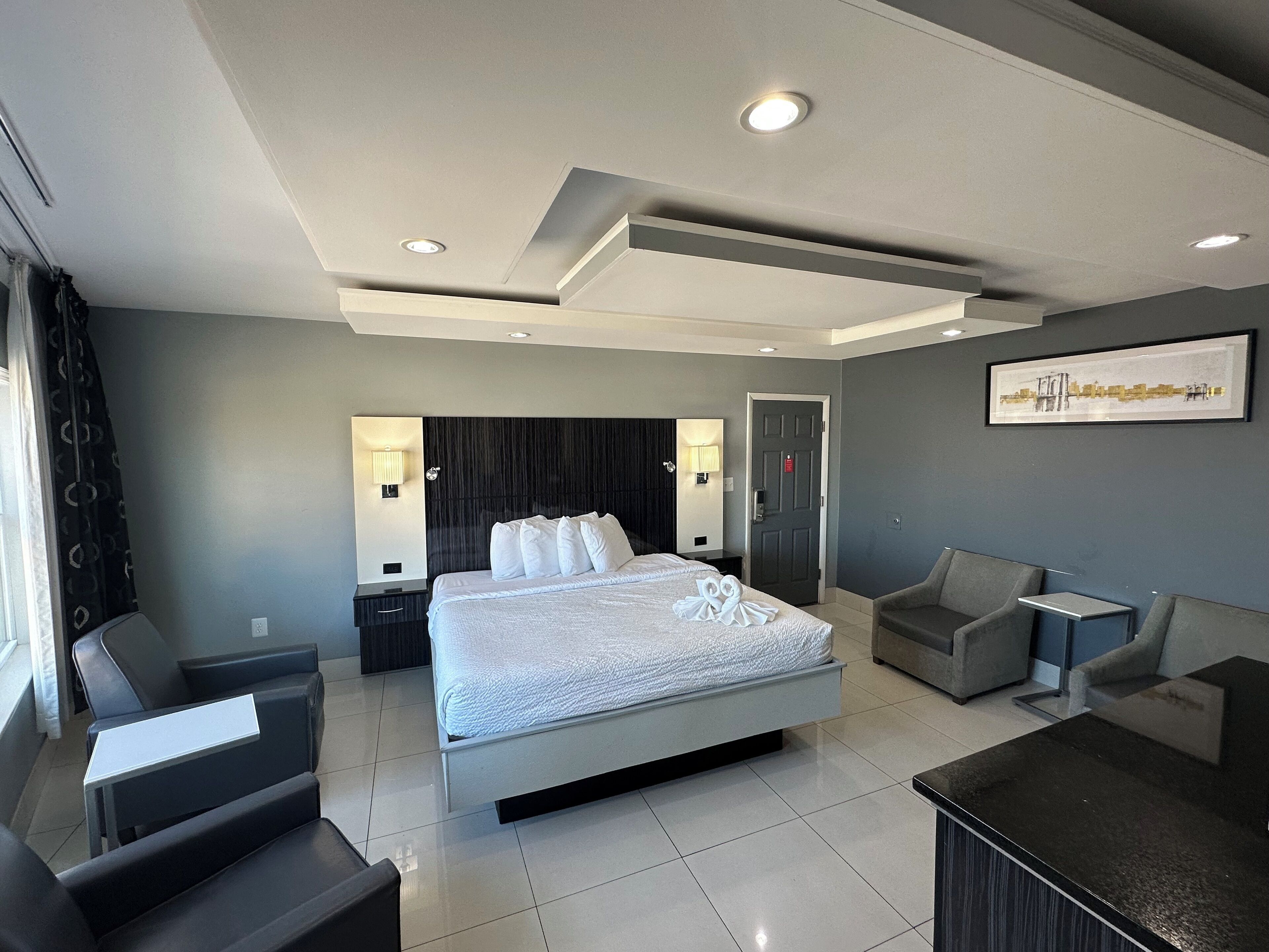 A modern hotel room with a large bed, two armchairs, a small table, and a painting on the wall.