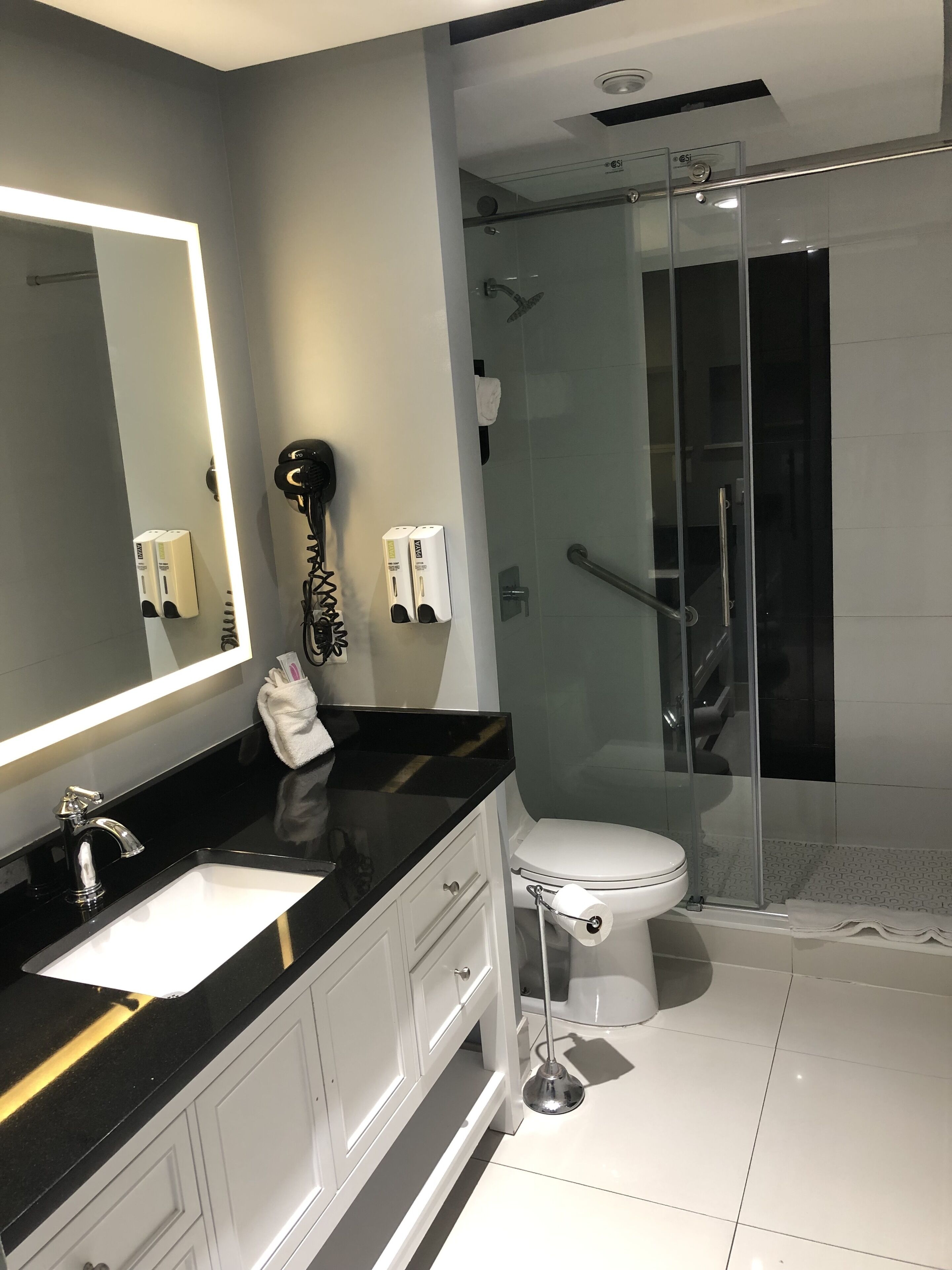 Een moderne badkamer met een zwart aanrecht, een witte wastafel en een douche met glazen wanden.