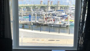 A view from a window of a marina with boats docked, a bridge in the background, and a 'NO SMOKING' sign on the pavement. - Marion Motor Lodge (St. Augustine)