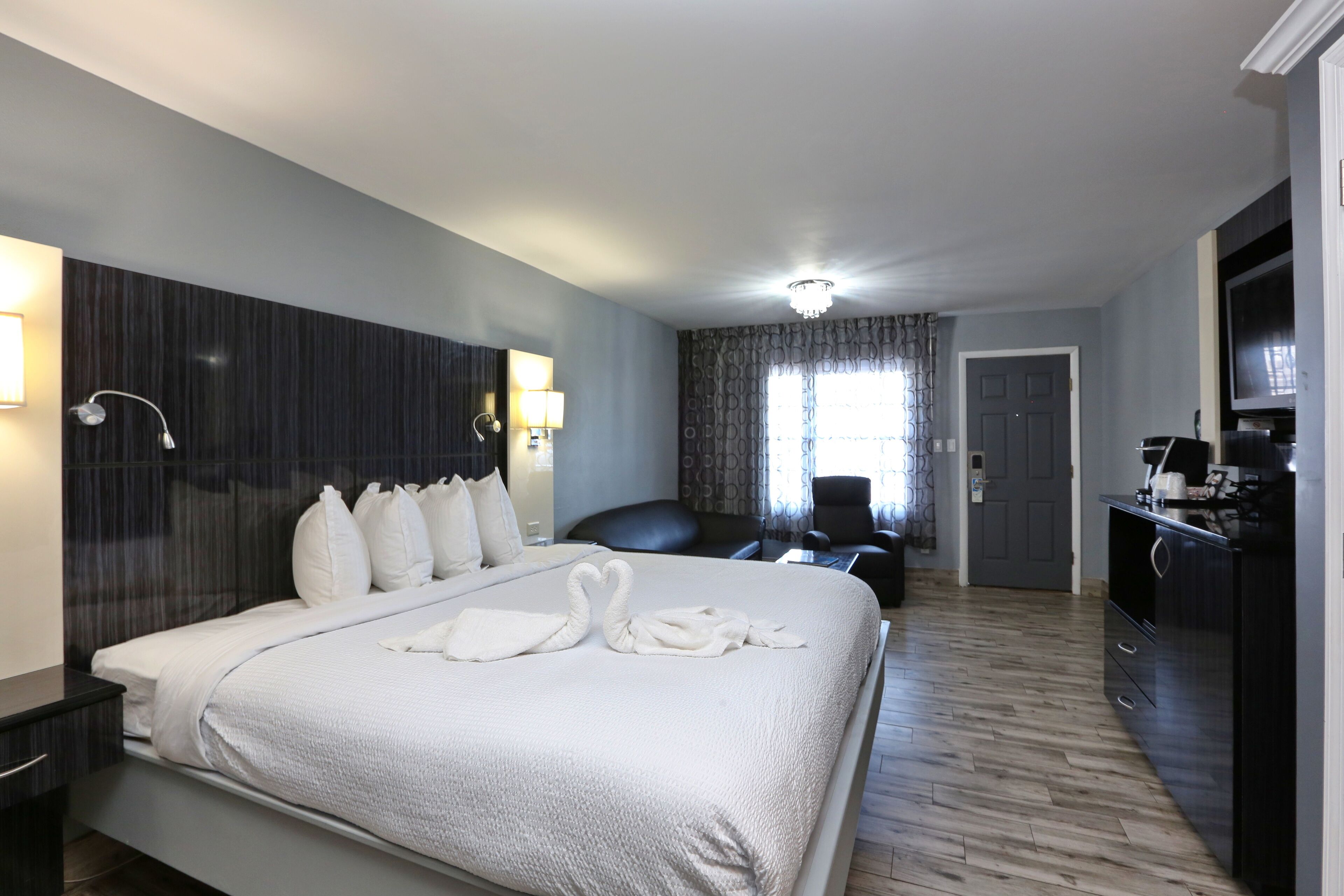 A hotel room with a large bed, a desk, a chair, a television, and a wardrobe.