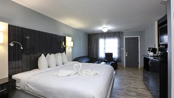 A hotel room with a large bed, a desk, a chair, a television, and a wardrobe.