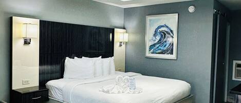 A modern hotel room with a large bed, bedside lamps, a painting on the wall, and a wooden floor.