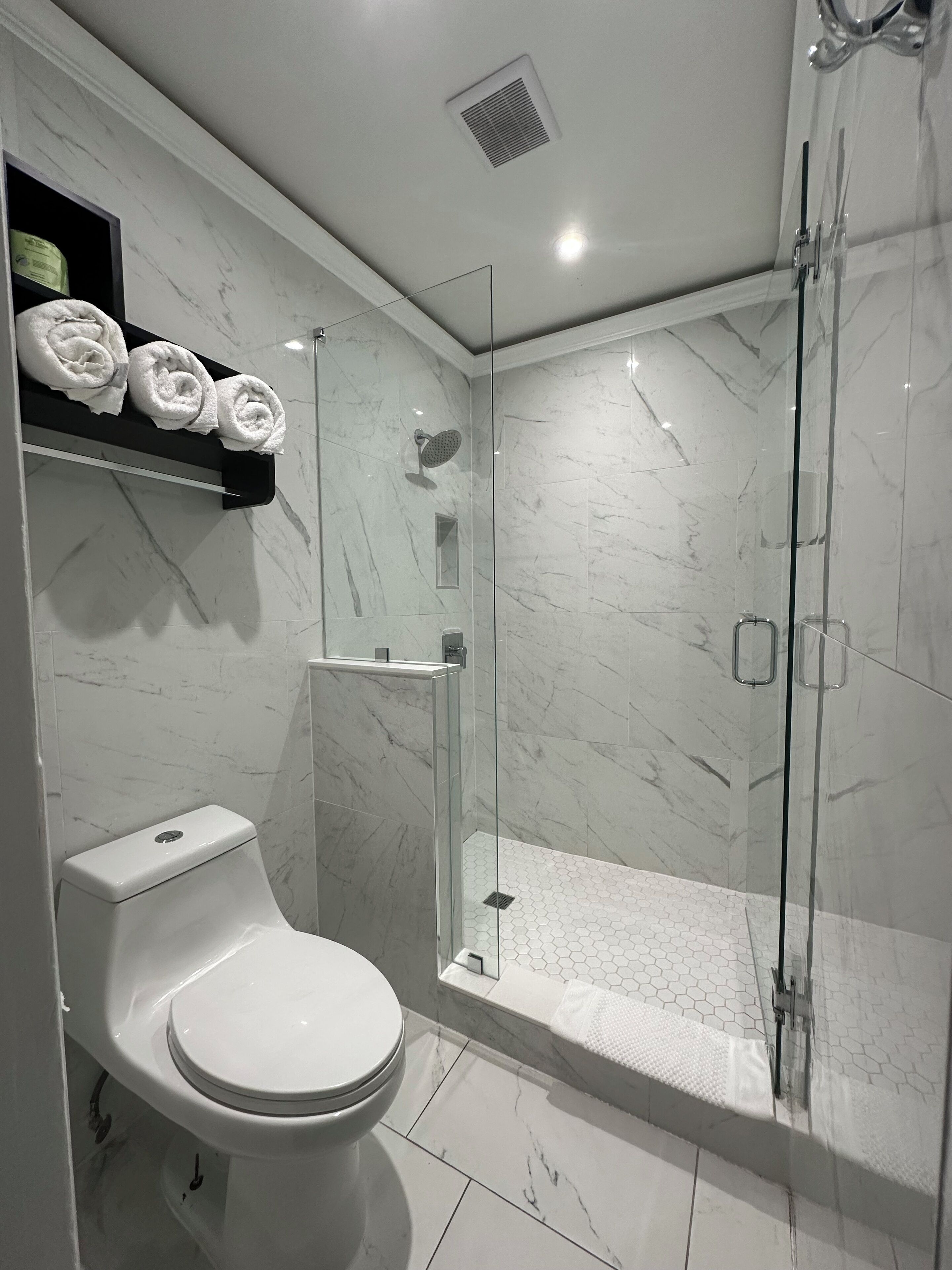 A modern bathroom with a toilet, a glass-enclosed shower, and a marble-tiled floor.