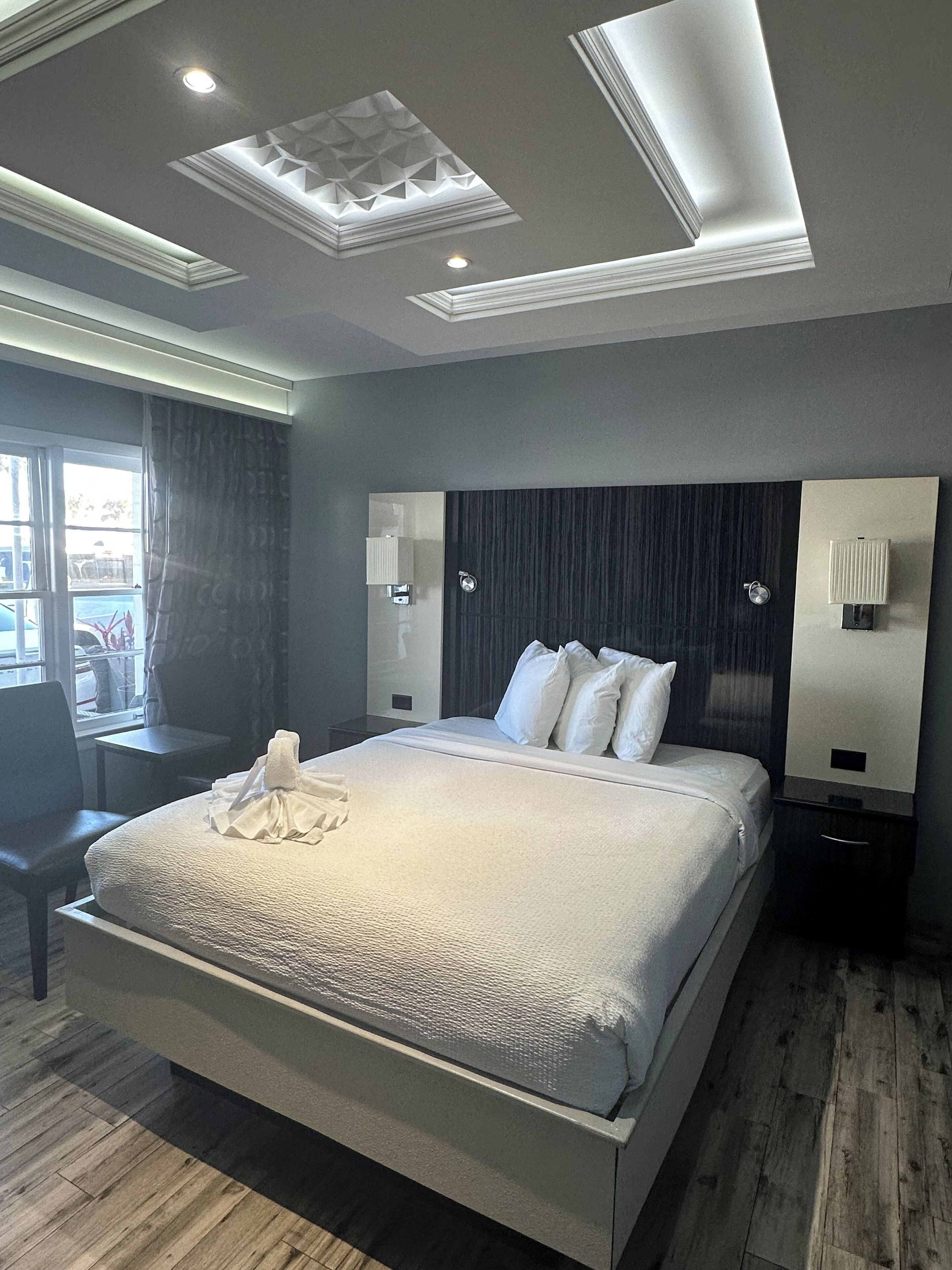 Una habitación de hotel moderna con una cama grande, mesitas de noche, un escritorio y vistas al exterior.