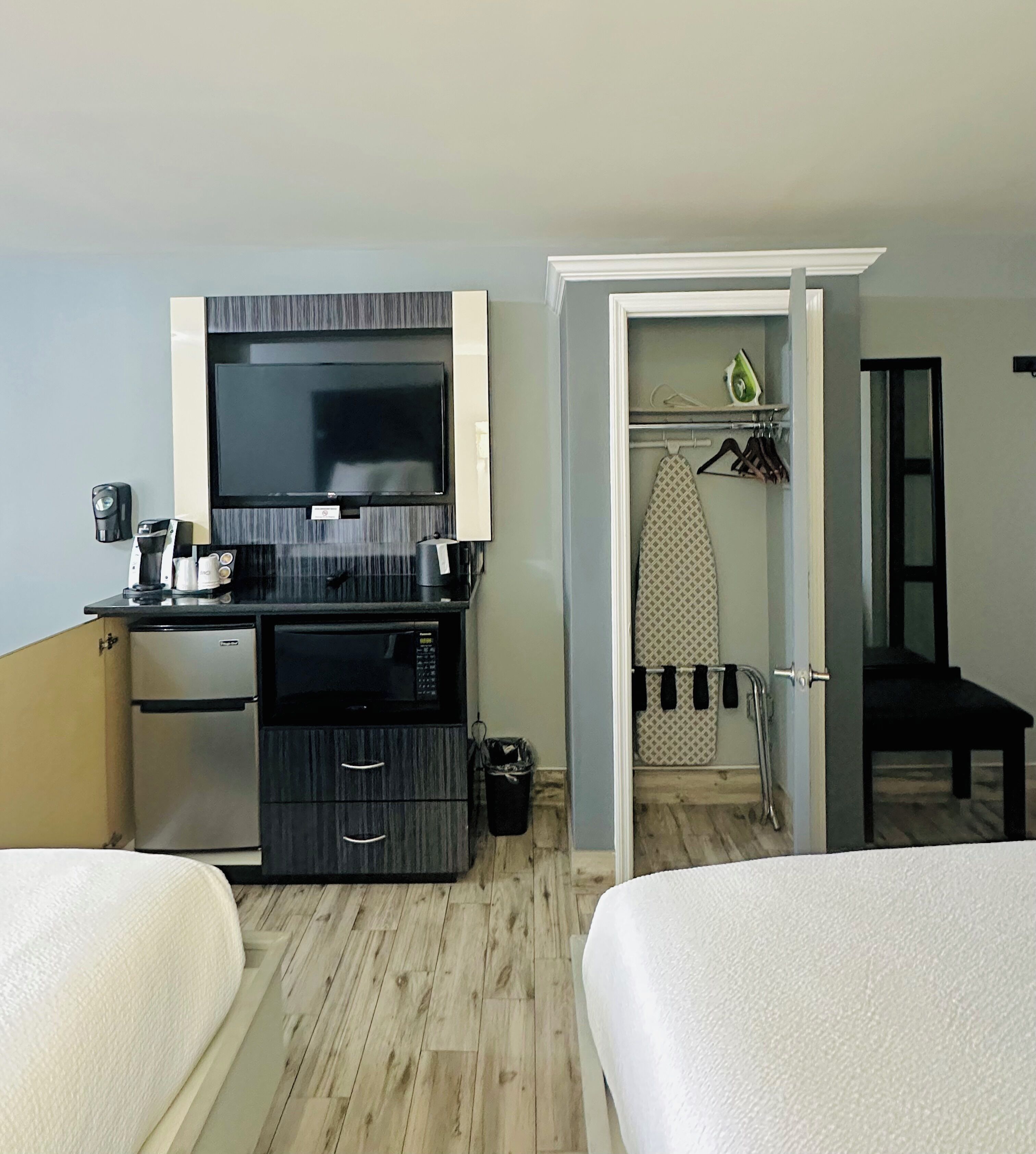 Quarto de hotel com duas camas, cozinha compacta equipada com micro-ondas, mini-frigorífico, televisão e banheiro com ferro e tábua de passar.