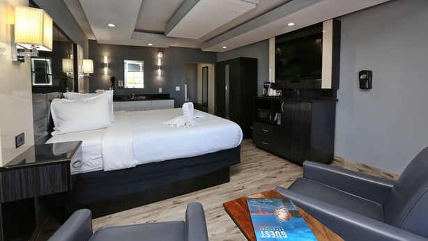 A modern hotel room with a large bed, a desk, a seating area, and a minibar. - Marion Motor Lodge (St. Augustine)