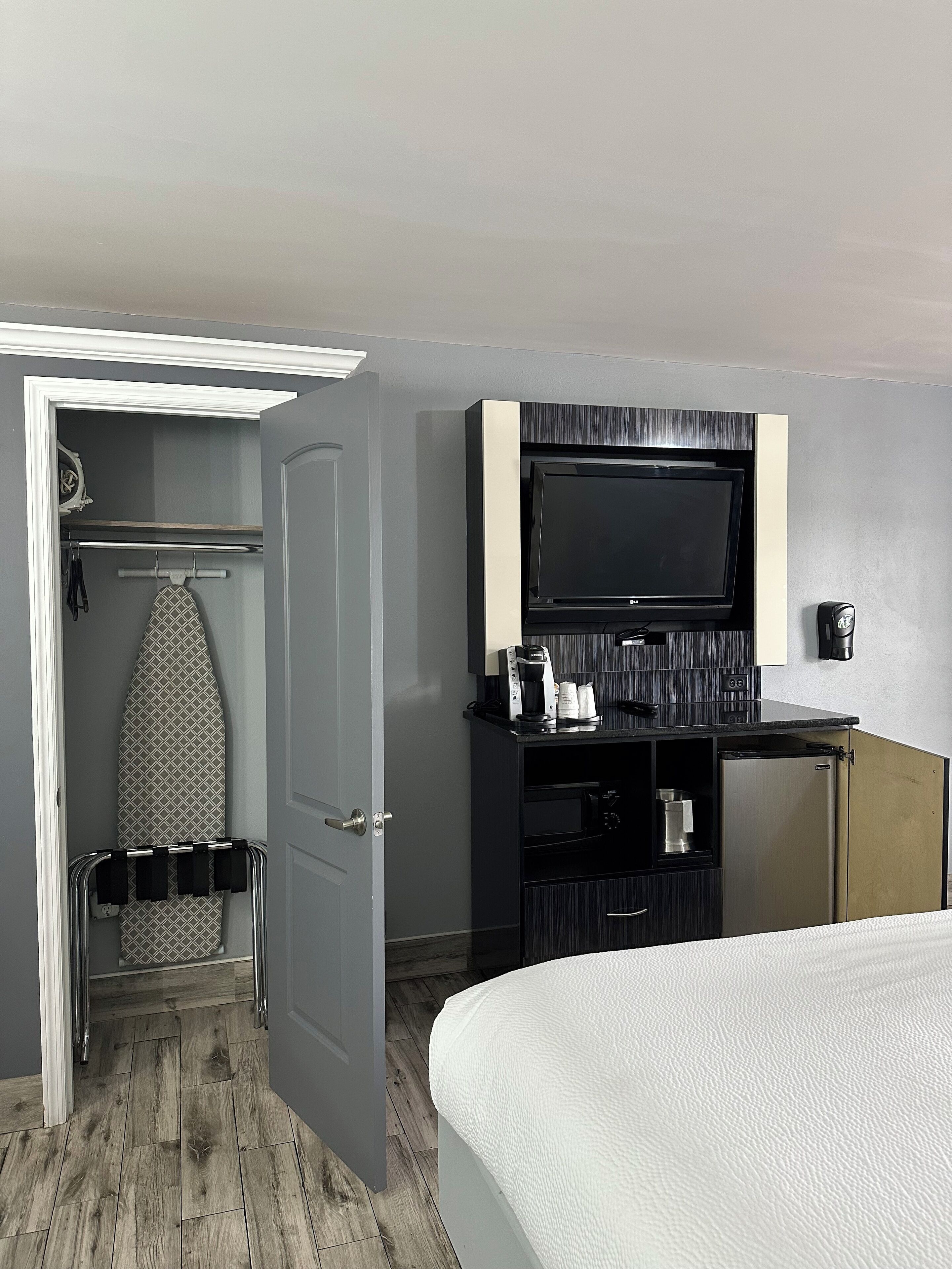 Ett hotellrum med en säng, en tv som är monterad på väggen, en minibar och en garderob med en strykbräda.