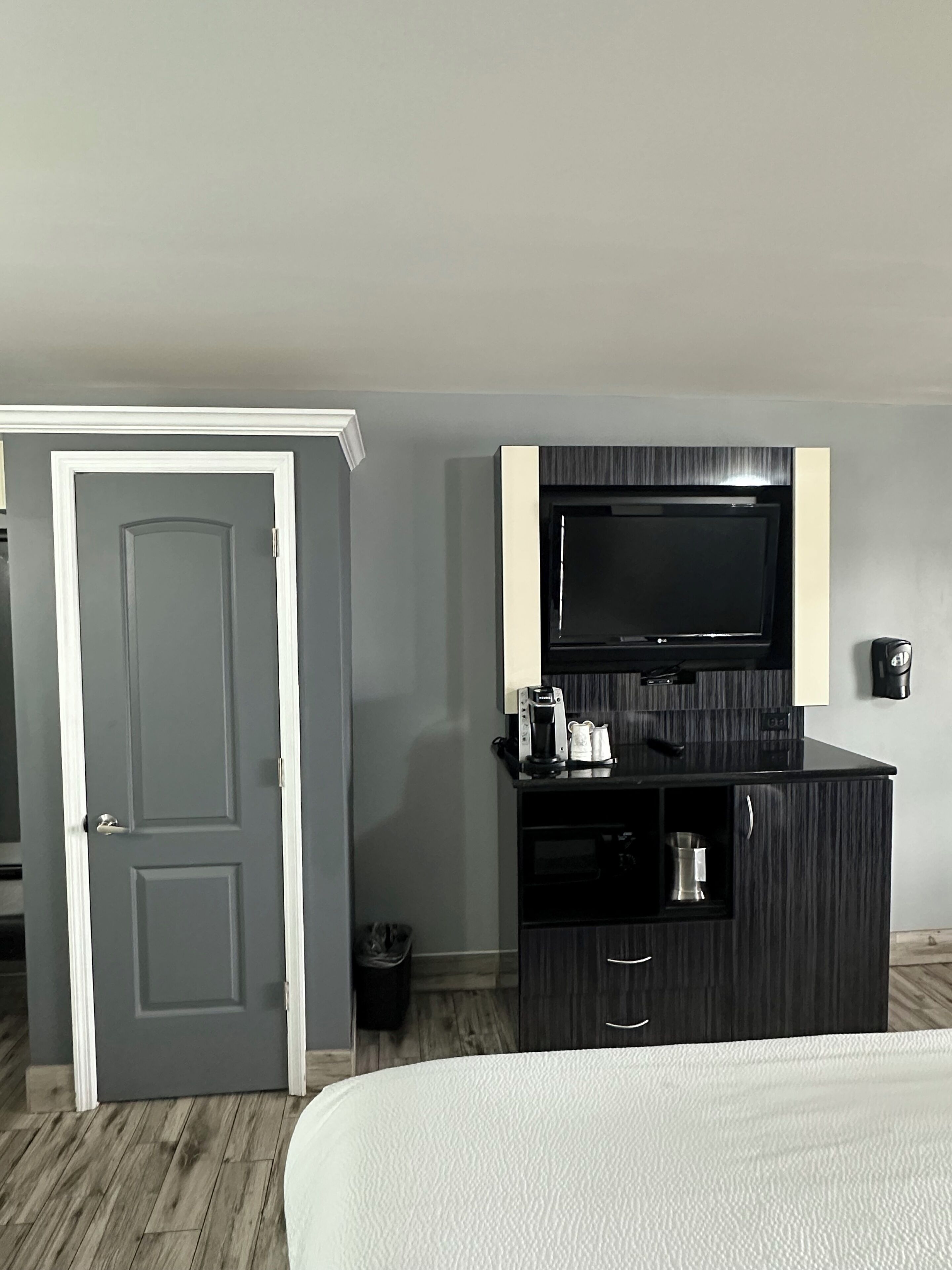 A hotel room with a bed, a dark wooden cabinet with a television, and a door.