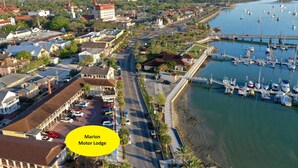 A marina with boats docked, a road with parked cars, and buildings with red roofs. - Marion Motor Lodge (St. Augustine)