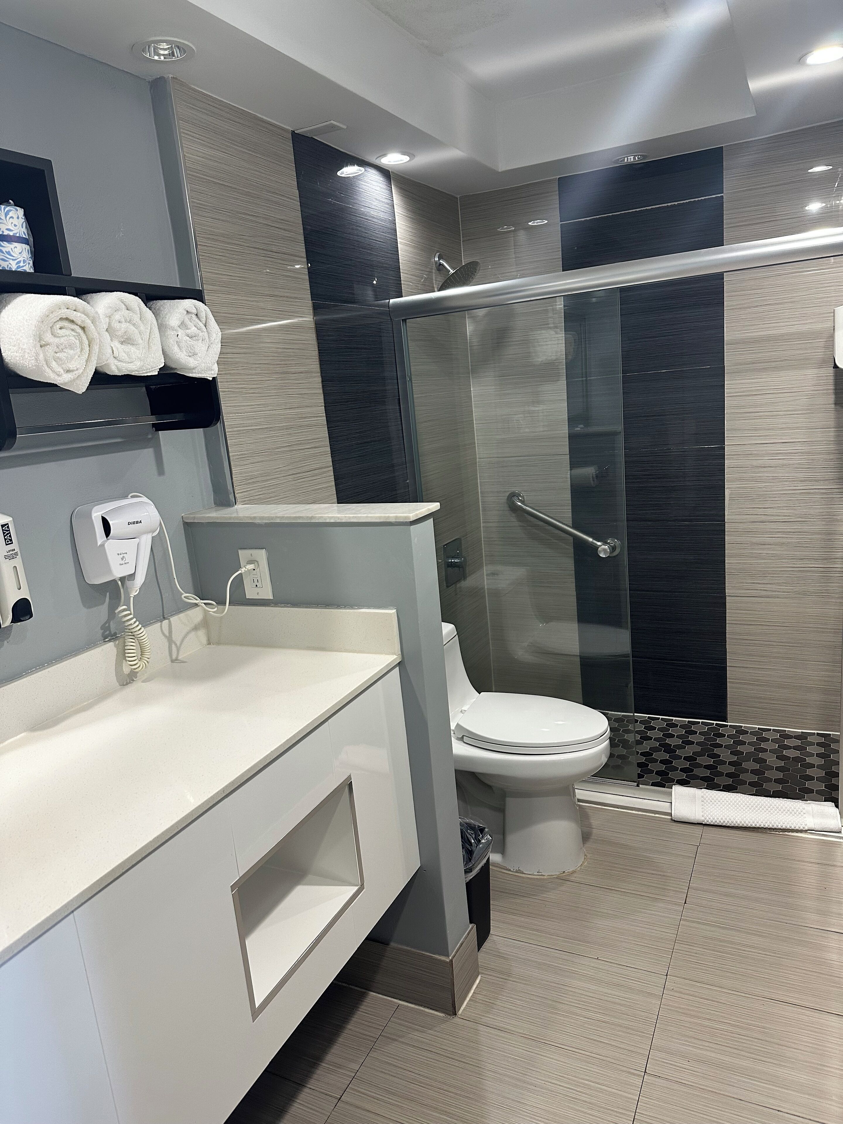 A modern bathroom with a glass shower enclosure, a toilet, and a vanity with a towel rack.