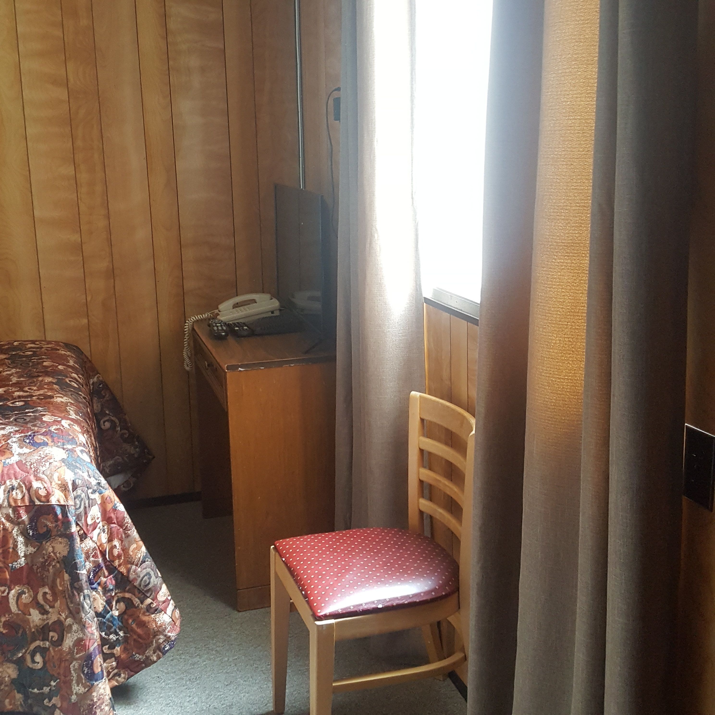 A room with a bed, a desk with a telephone, and a chair.