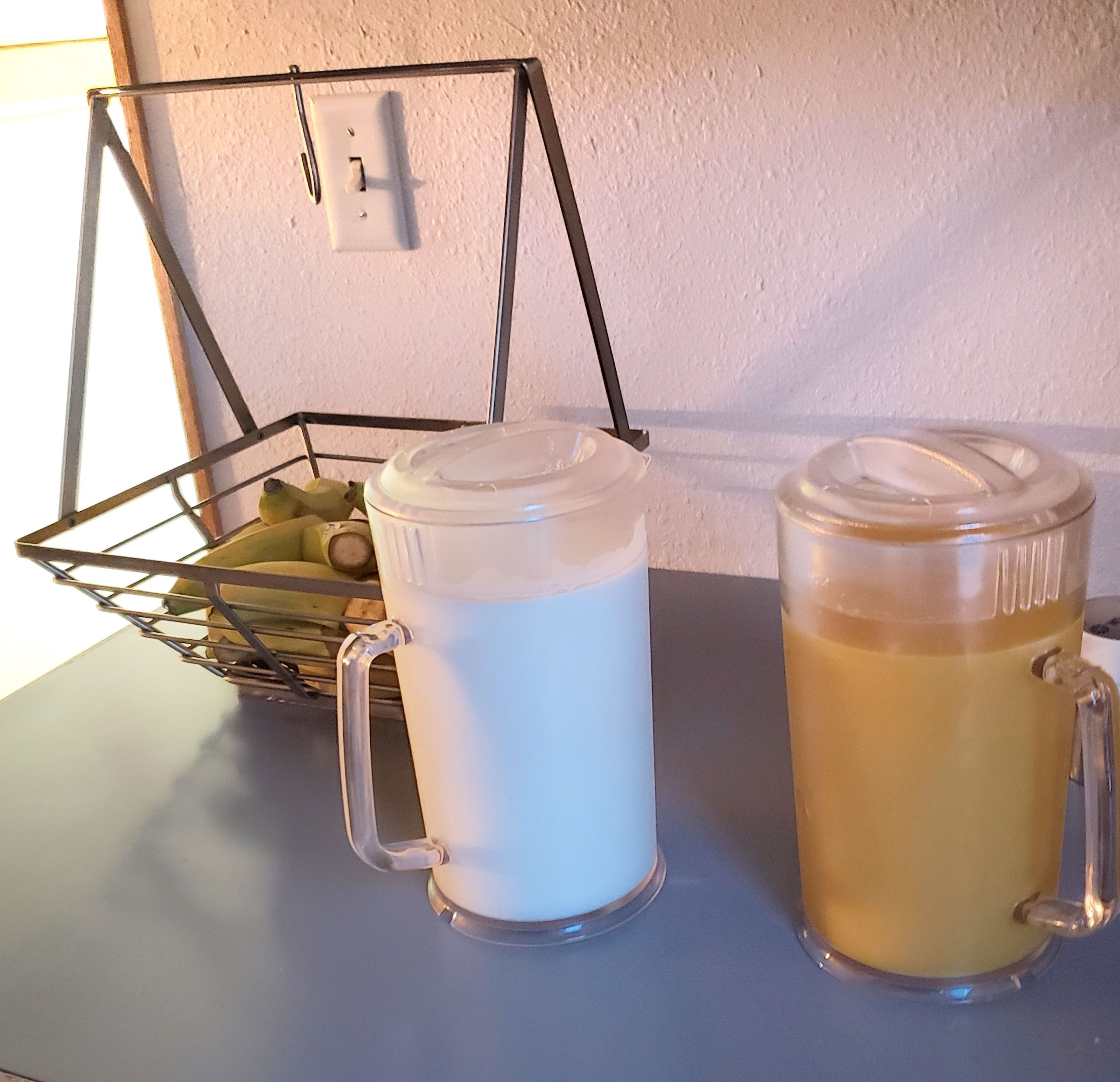 Zwei Glasbecher auf einem Tisch mit einem Drahtkorb, der Früchte enthält.