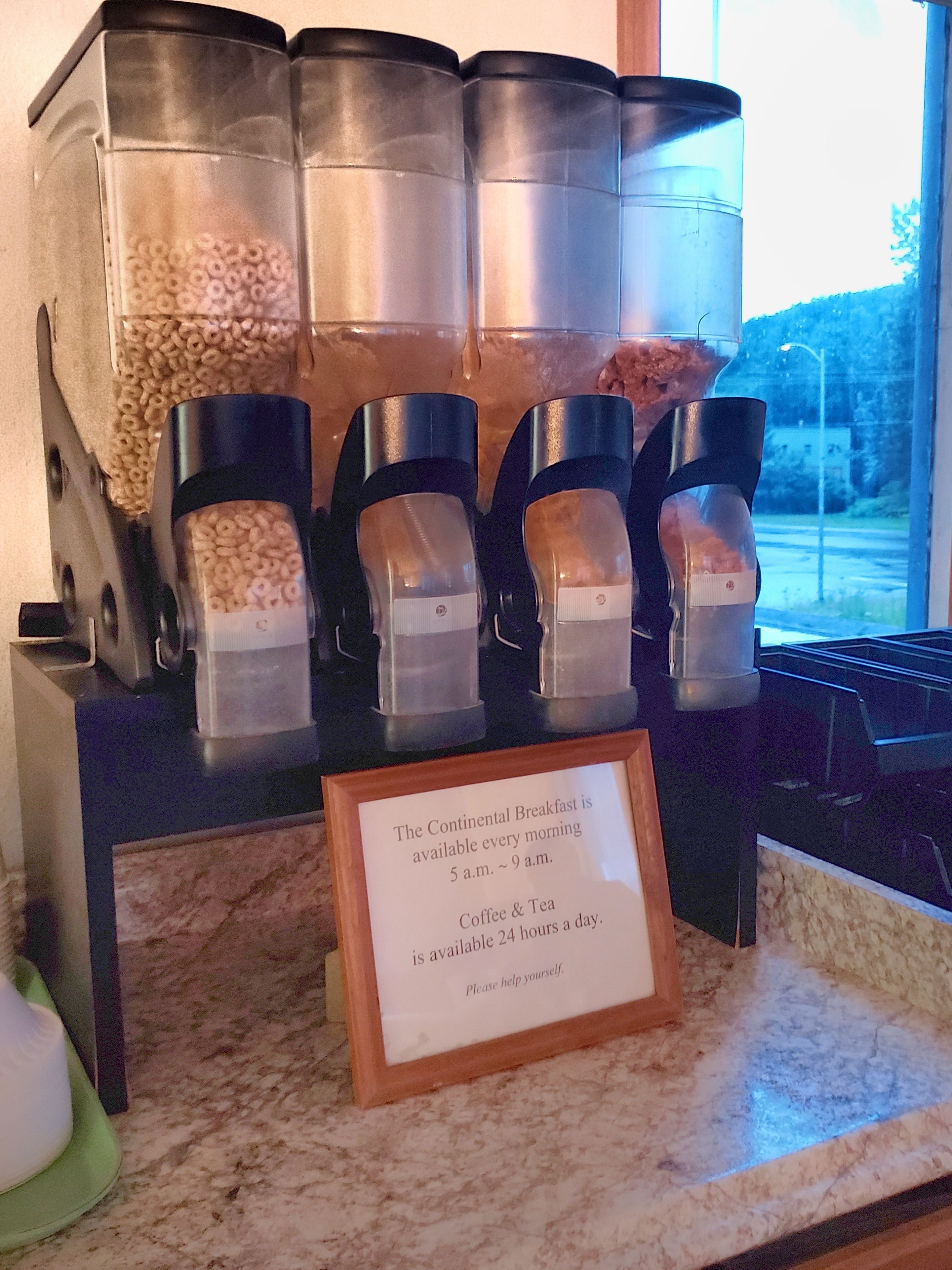A breakfast station with containers of cereal and coffee, and a sign indicating breakfast availability.