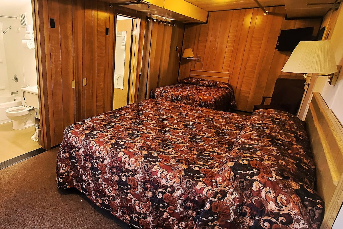A bedroom with two beds, a bathroom with a shower, and a wooden ceiling.