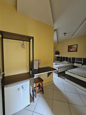 Una habitación compacta con cama, escritorio, silla y un refrigerador pequeño.
