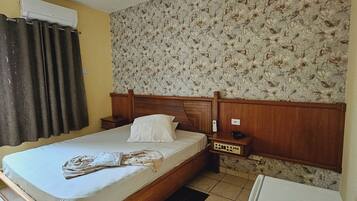 Een slaapkamer met een bed, een nachtkastje, een wandairconditioner, een koelkast en behang met een patroon.