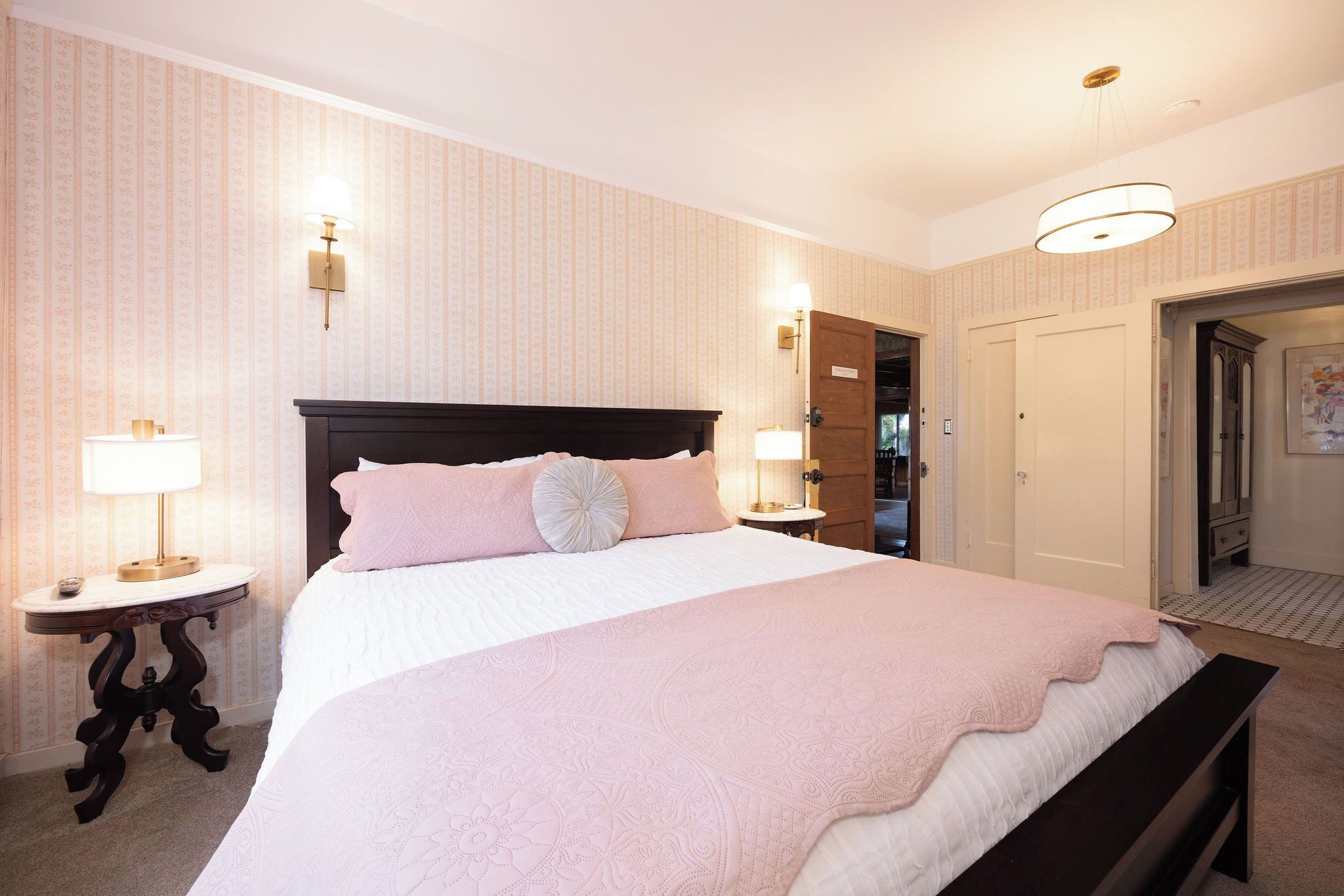 Une chambre d’hôtel avec un grand lit, deux tables de chevet avec des lampes, une armoire et une porte donnant sur une autre pièce.