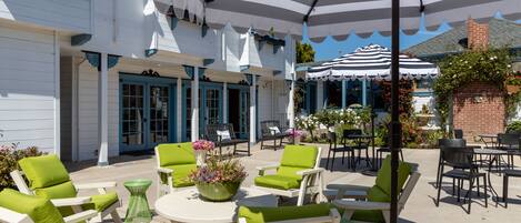 Une terrasse extérieure avec des meubles blancs et verts, des parasols à rayures et un mur de briques.