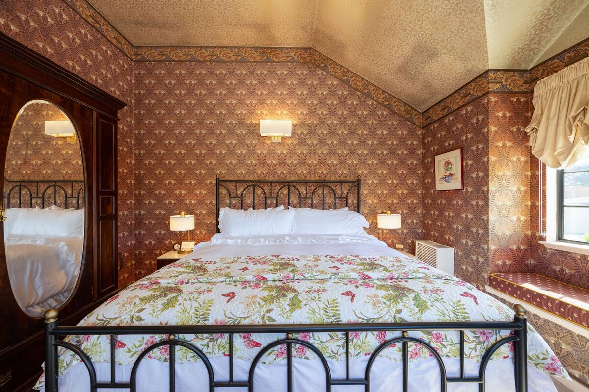 Una camera da letto con un letto grande, due lampade da comodino, uno specchio e una finestra con tende.