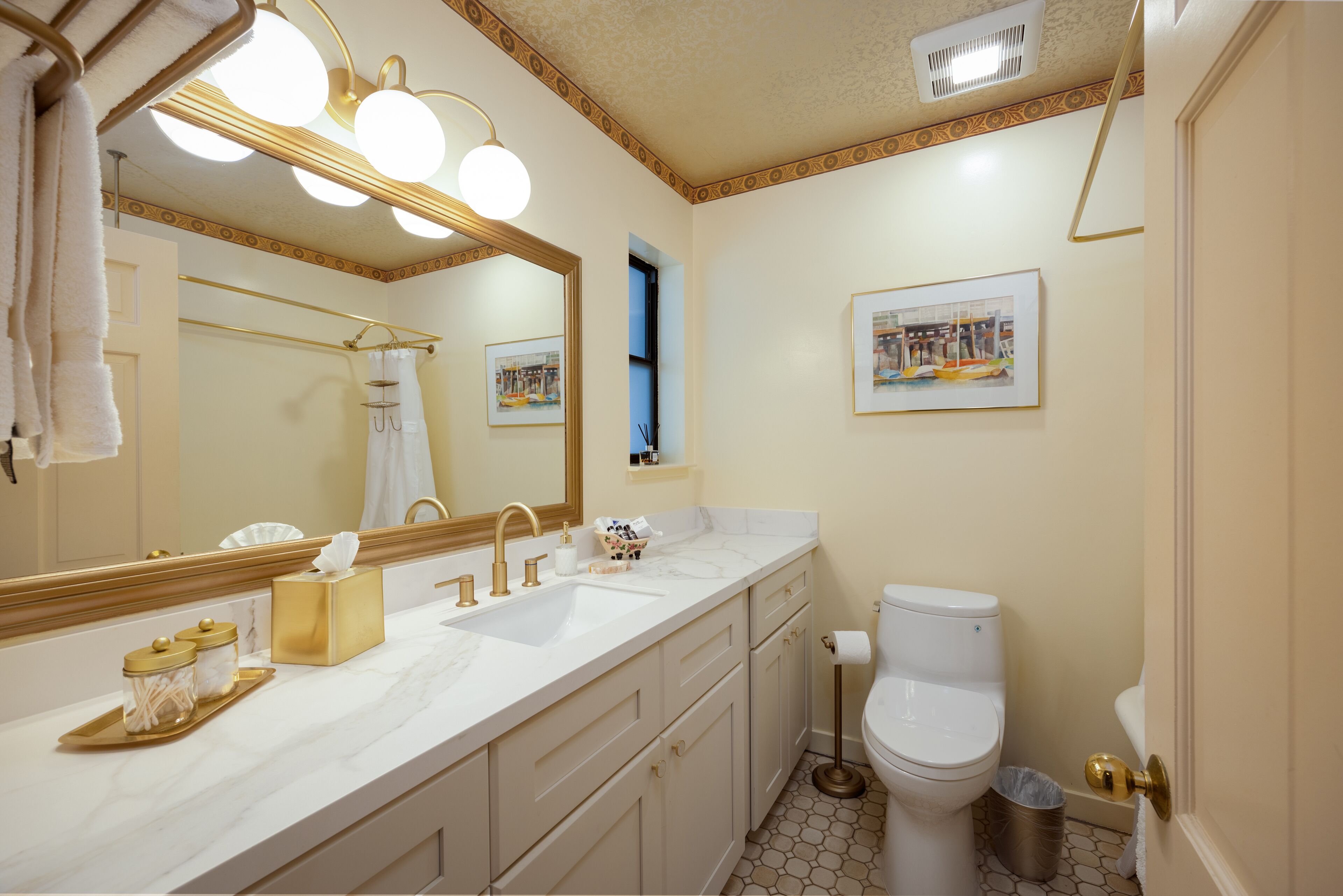 A bathroom with a large mirror, two sinks, a toilet, and a trash can.
