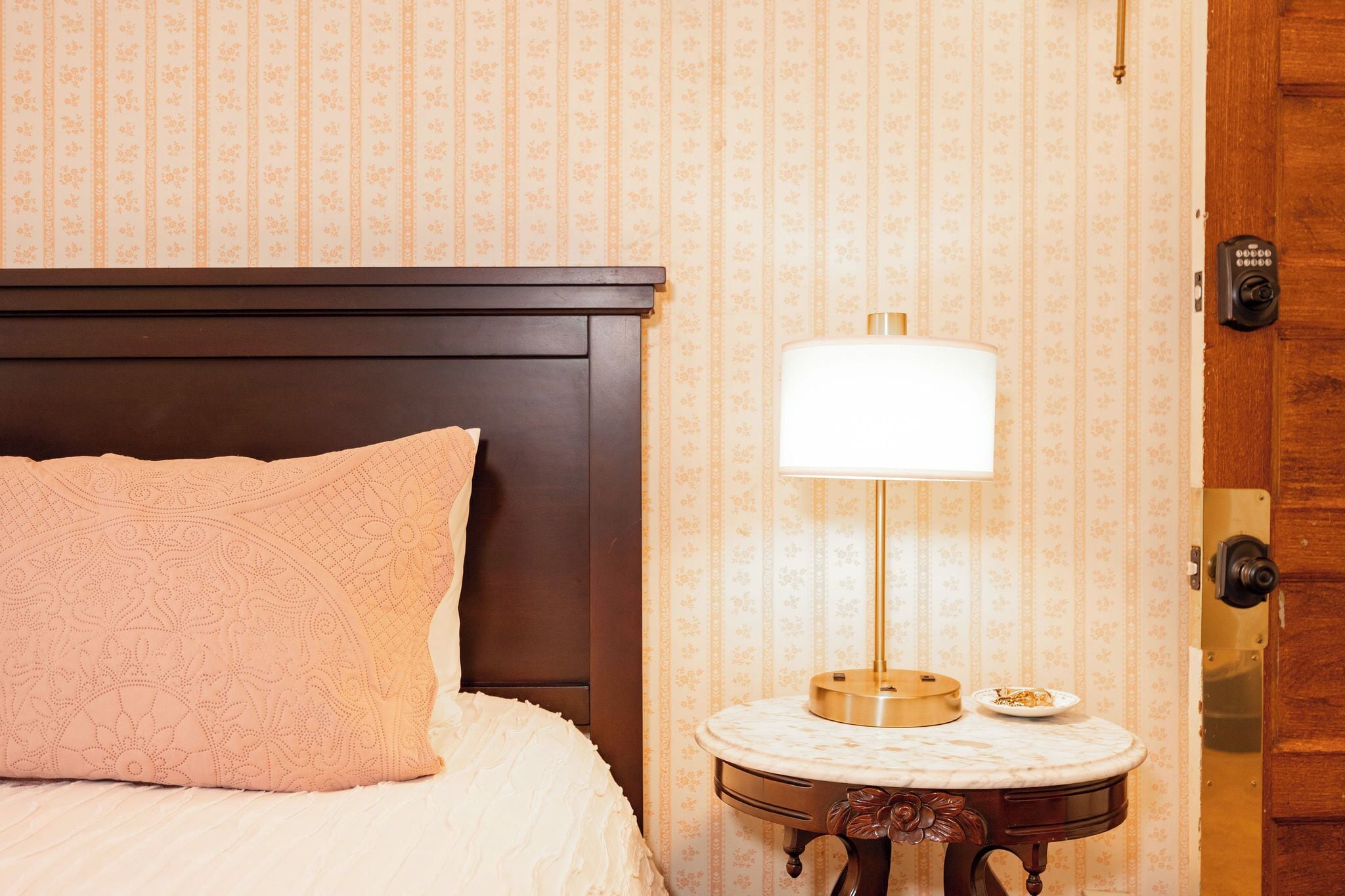 A hotel room with a bed, a nightstand with a lamp, and a door.