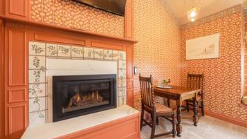 A dining area with a fireplace, patterned wallpaper, and a wooden dining table.