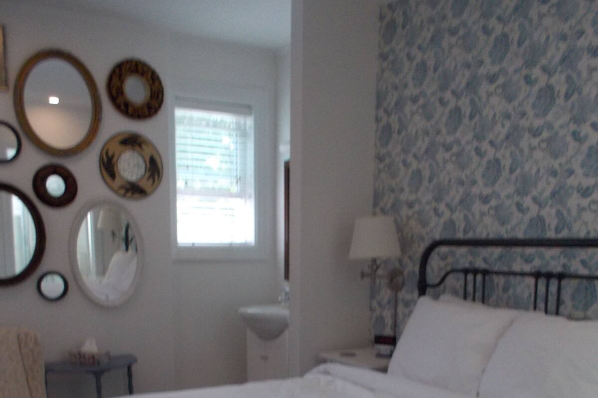 A bedroom with a large bed, a bedside table, a lamp, and a wall decorated with circular mirrors.