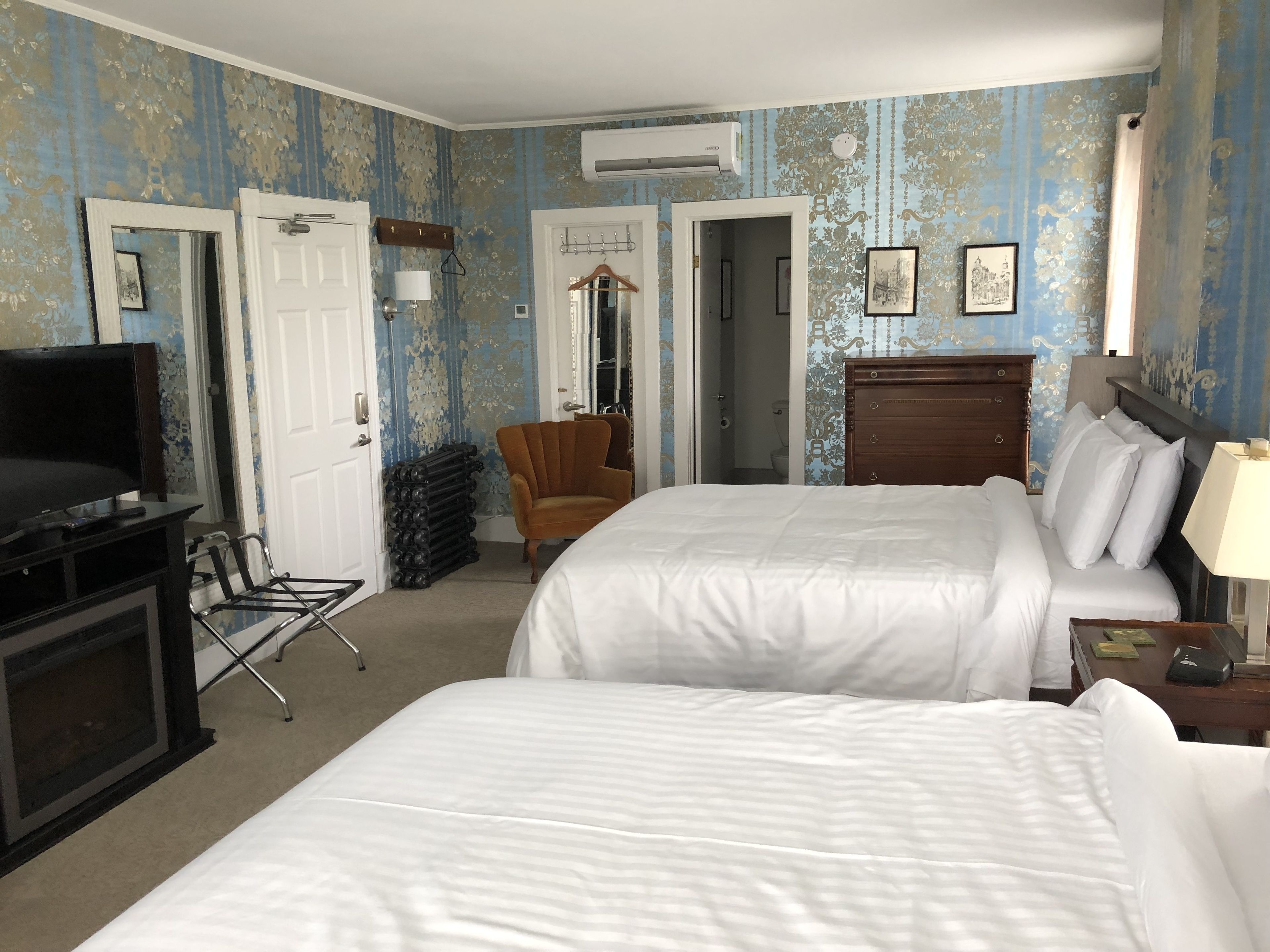 A hotel room with two beds, a TV, a chair, and a wardrobe.