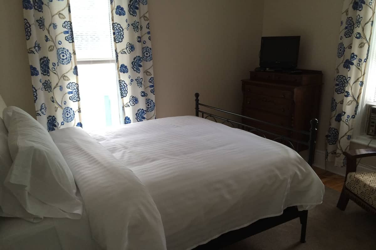 A bedroom with a bed, a wooden dresser, and a television on top.