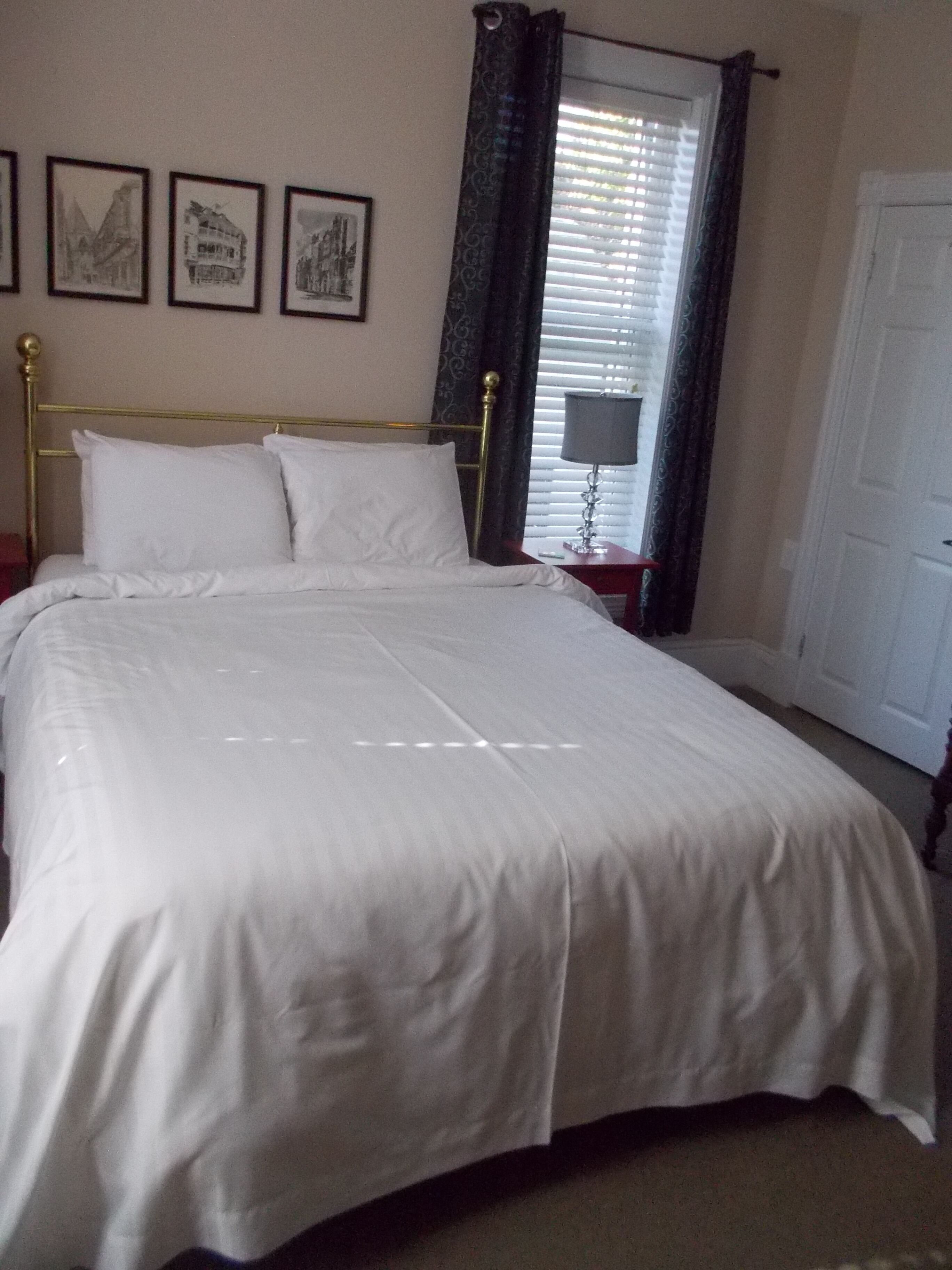 A neatly made bed with white linens, a gold-framed headboard, and a window with curtains.