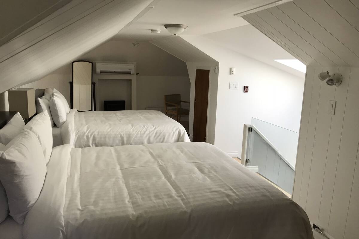 A bedroom with two beds, a ceiling fan, an air conditioning unit, and a view of the outside through a window.