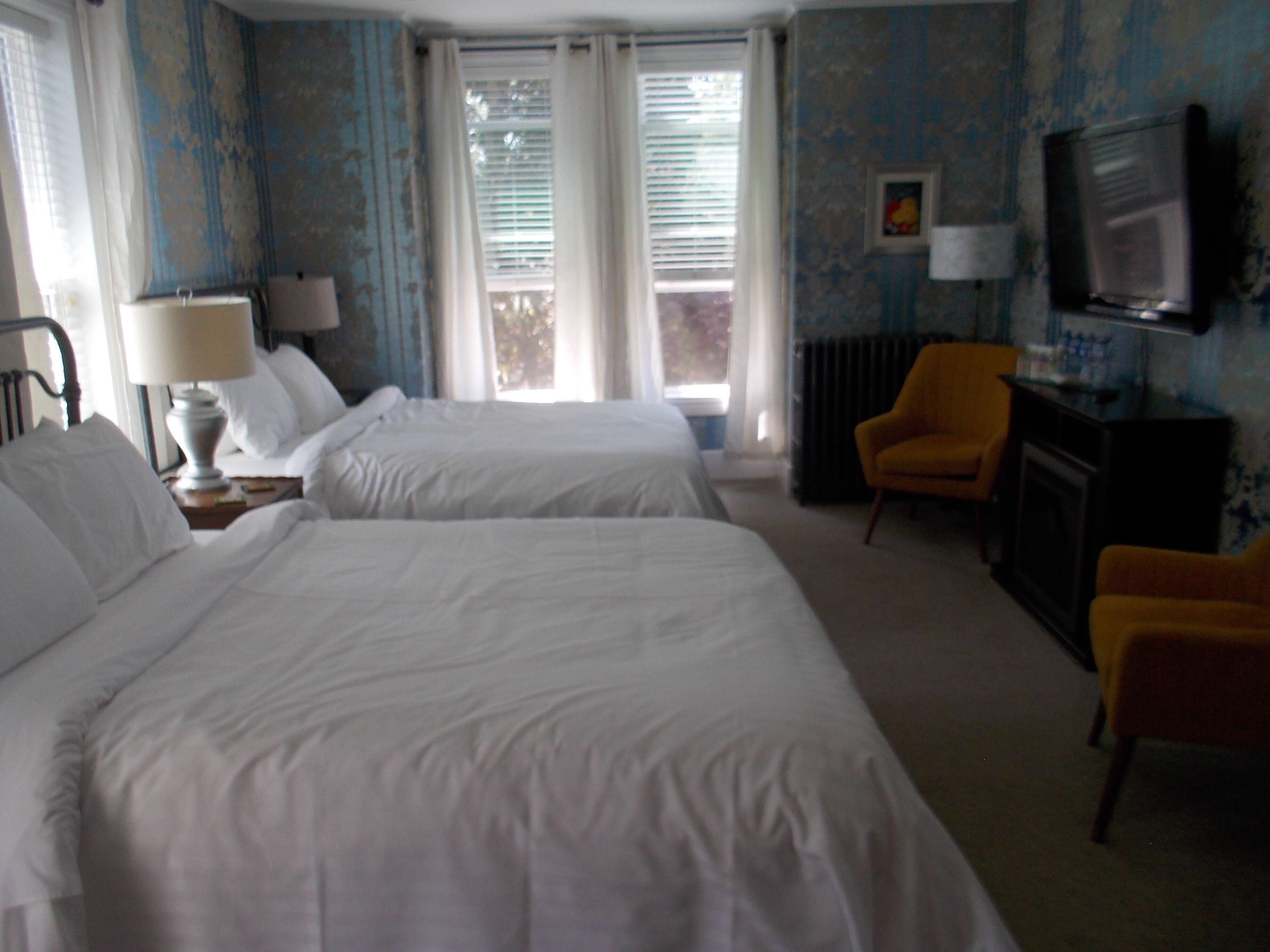 A hotel room with two beds, a television, a chair, and a radiator.
