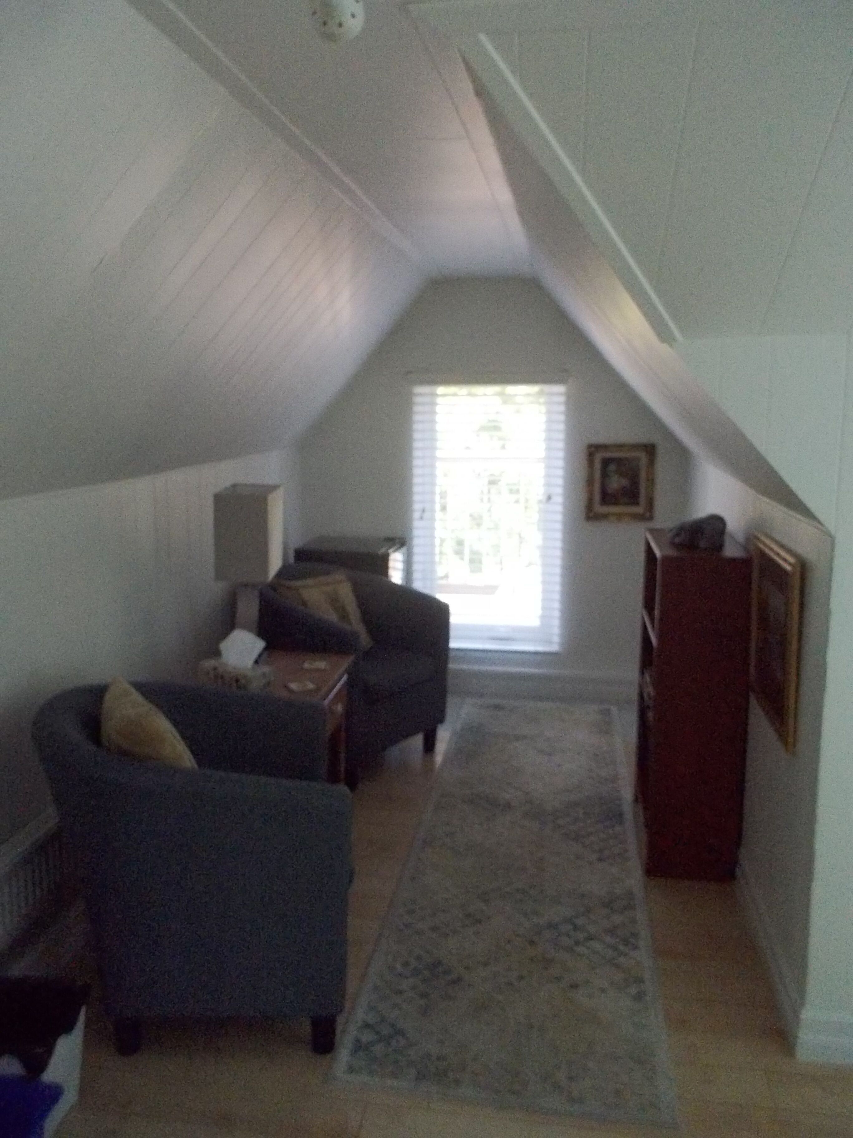 A cozy attic bedroom with a sloped ceiling, a dark blue sofa, a small table, and a wooden cabinet.