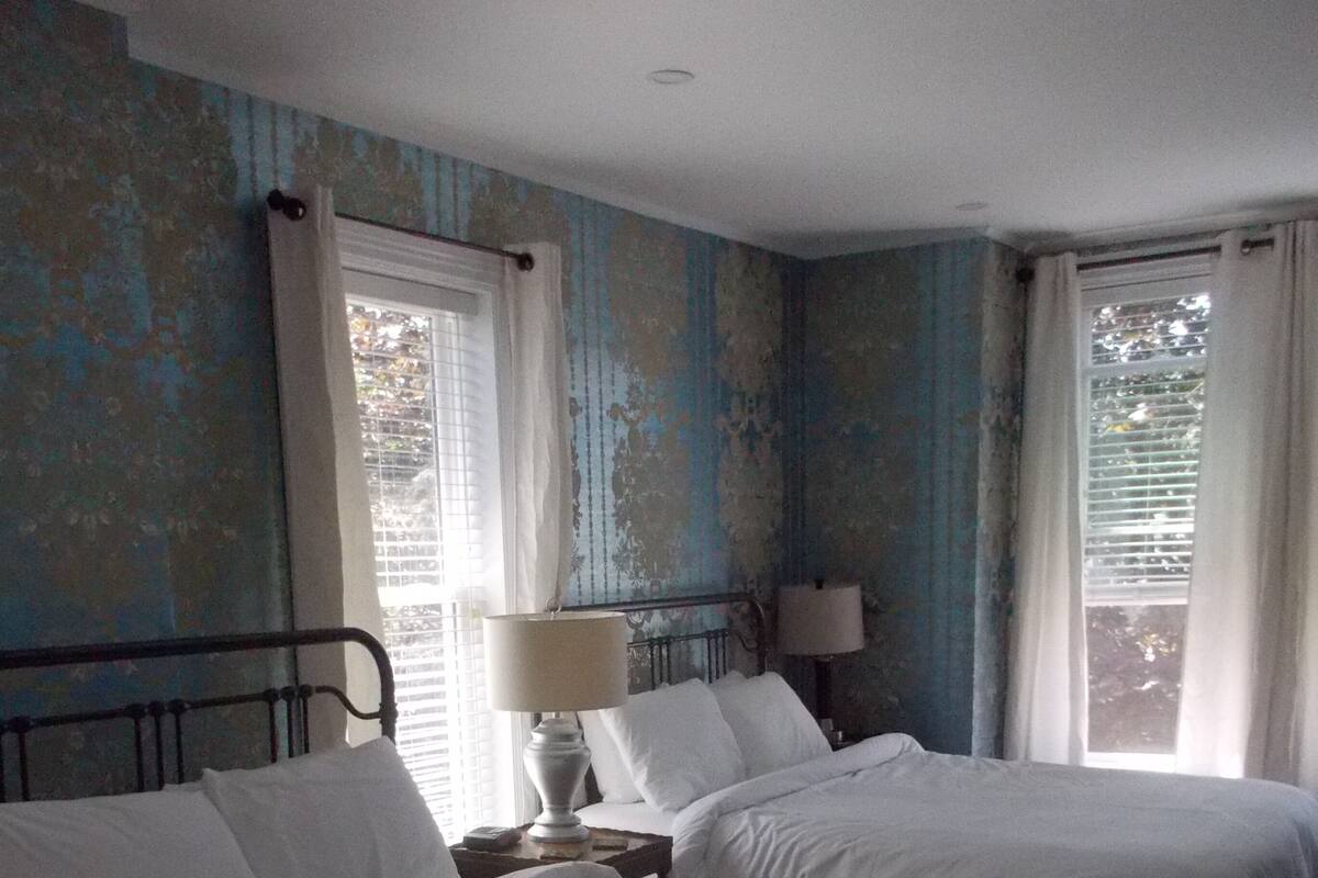 A room with two beds, a nightstand with a lamp, and a window with curtains.
