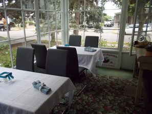 Un restaurant avec des tables dressées, de grandes fenêtres donnant sur la rue et une enseigne indiquant le nom de l’établissement.