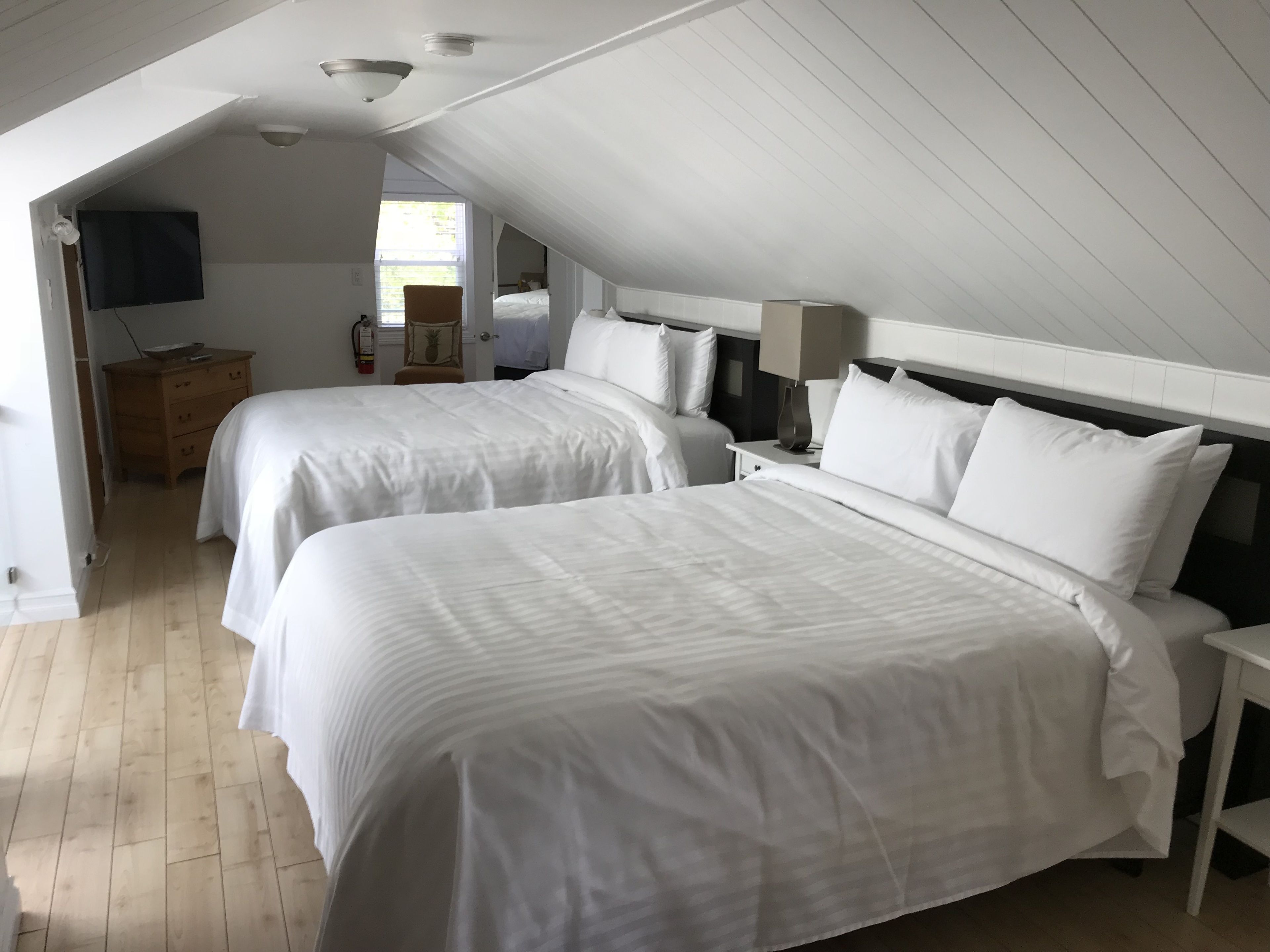 A hotel room with two beds, a wooden dresser, a TV, and a window with natural light.
