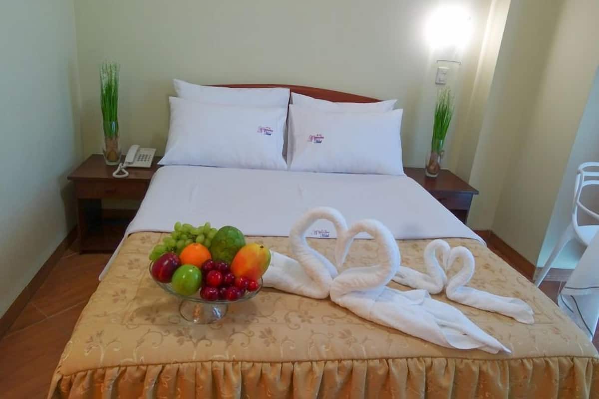 Quarto de hotel com cama bem arrumada, uma cesta de frutas sobre a cama e telefone na mesinha de cabeceira.