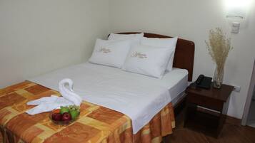 Una cama bien hecha con sábanas blancas, un frutero sobre la cama y un florero con flores secas en la mesita de noche.