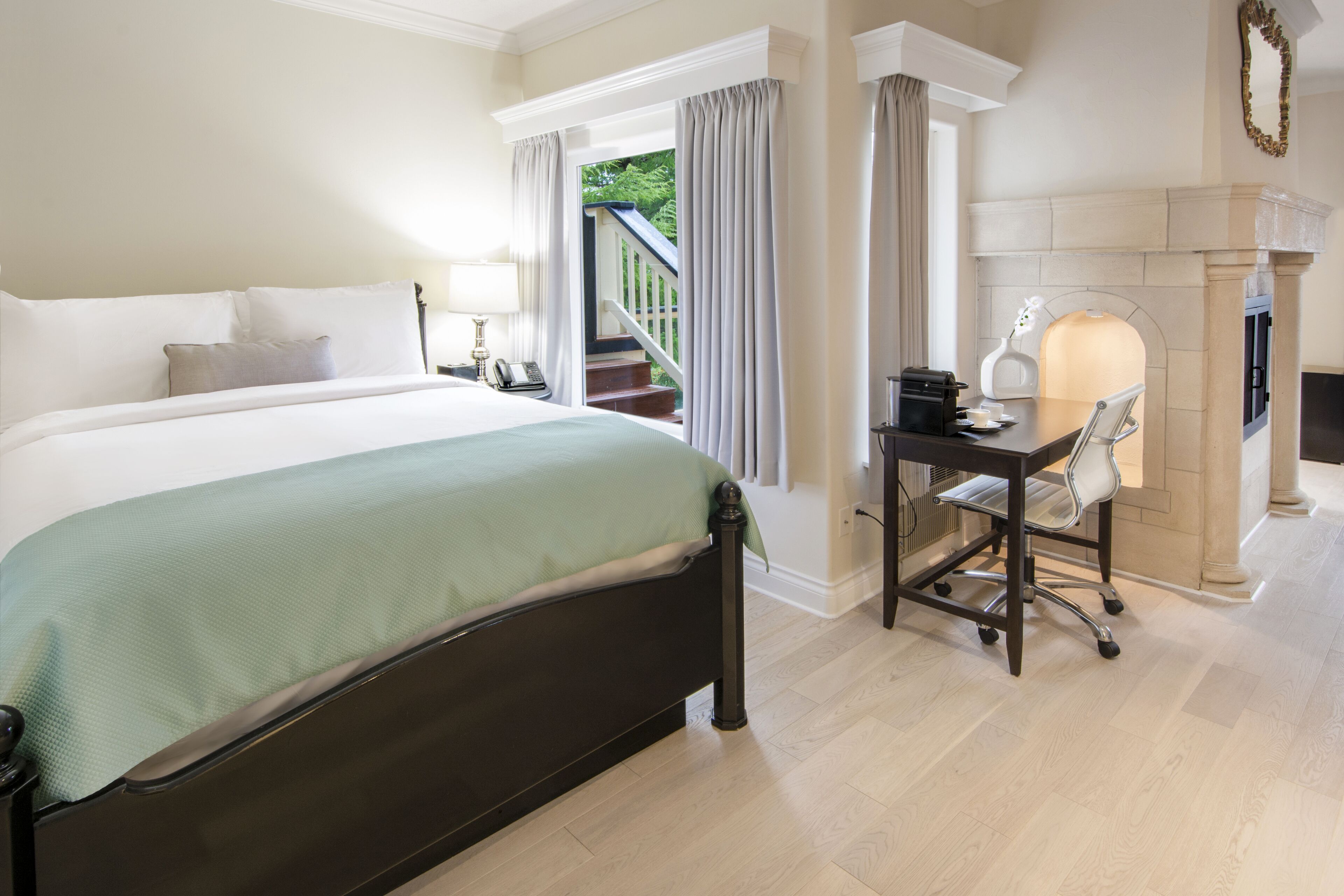 A hotel room with a large bed, a desk with a chair, a fireplace, and a view of a staircase leading to a balcony.