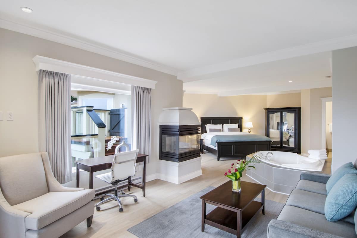 A modern hotel room with a sofa, armchair, dining table, and a large bed.