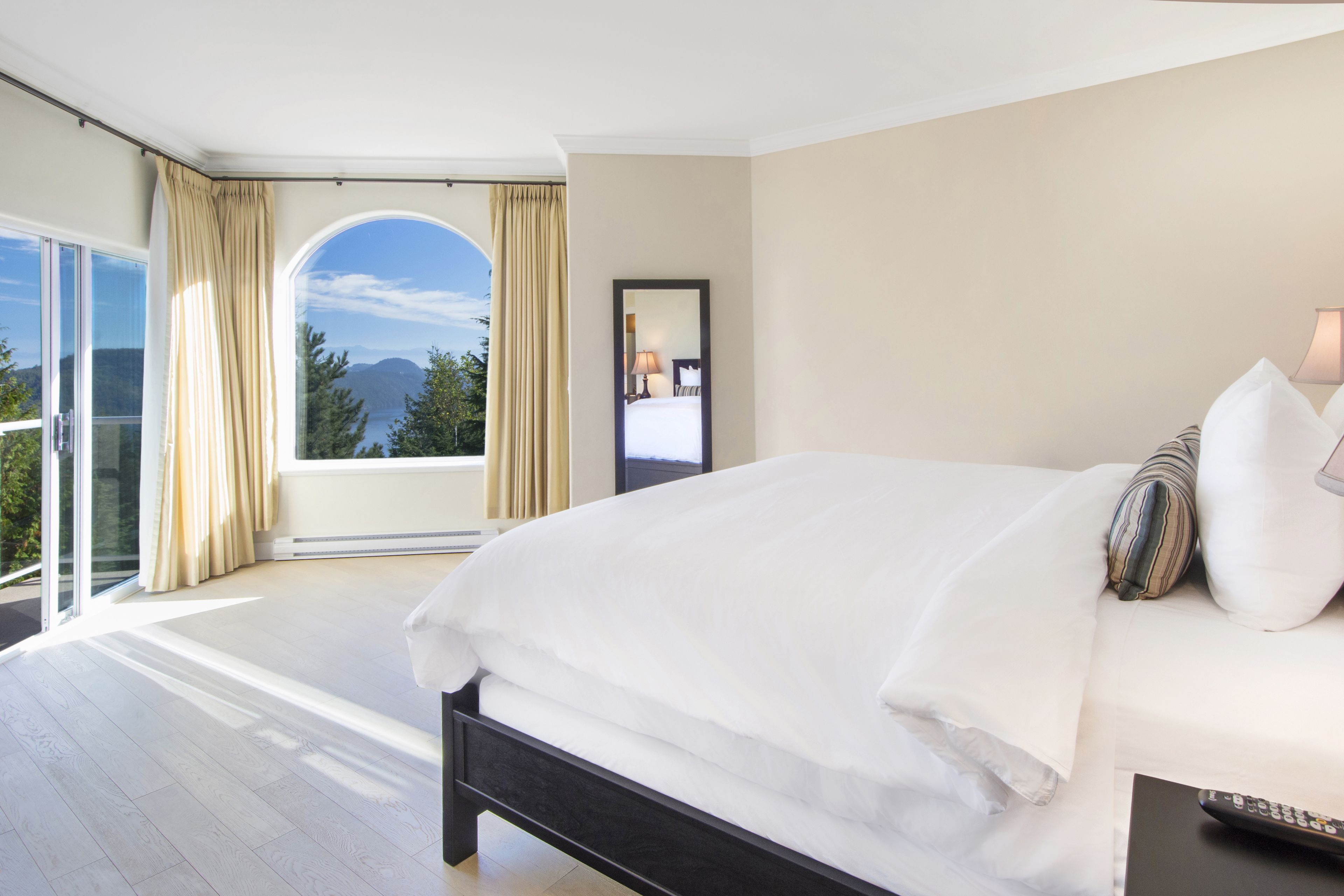 Quarto com cama grande, varanda com cortinas e vista para montanhas.