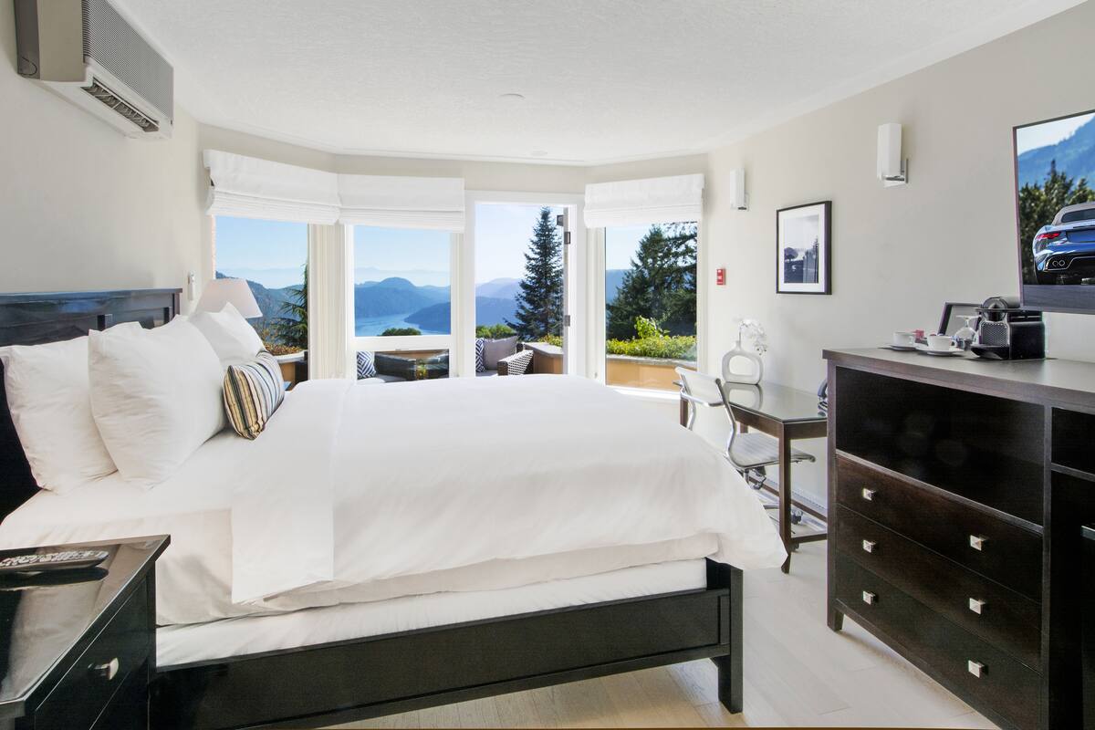 A modern hotel room with a large bed, a desk, and a view of mountains.