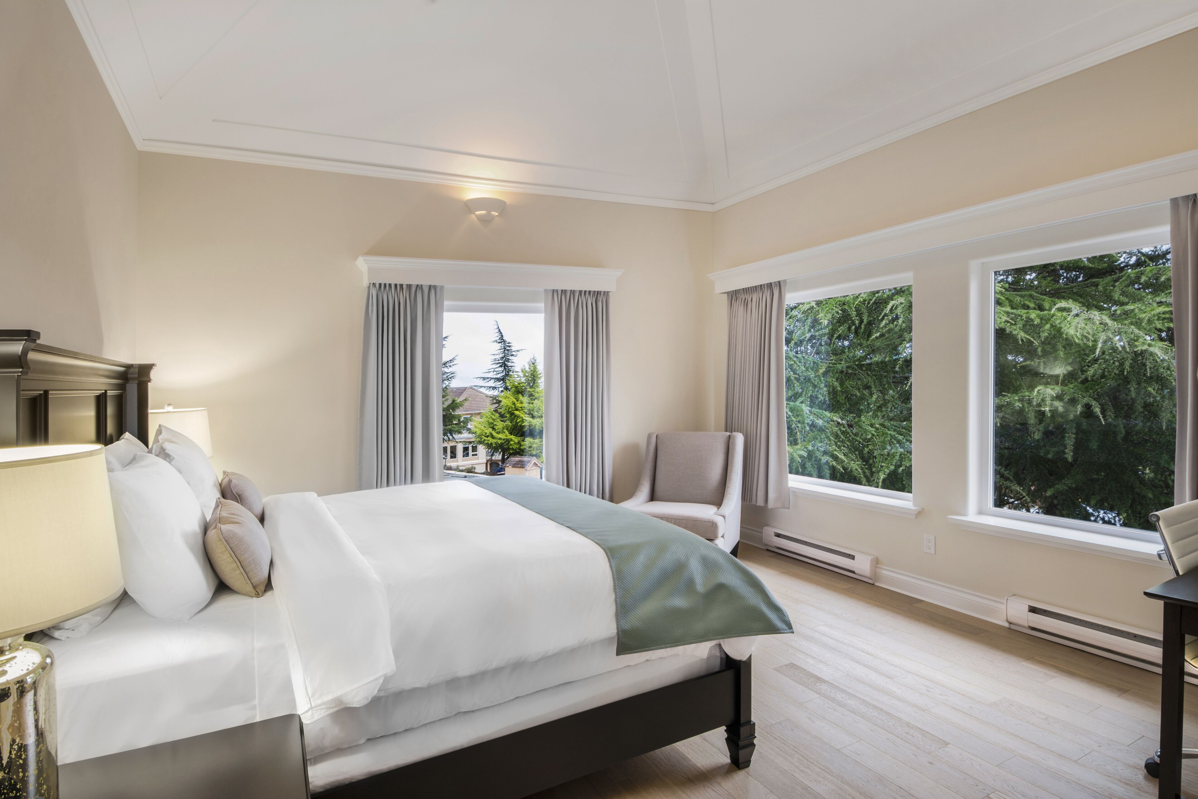 A bedroom with a bed, a chair, and large windows.