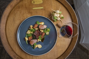 A wooden table with a blue plate of food, a glass of red wine, and a wooden sign. - Villa Eyrie Resort (Malahat)