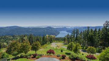 A scenic view of a mountainous landscape with a winding road, lush greenery, and a lake in the distance.