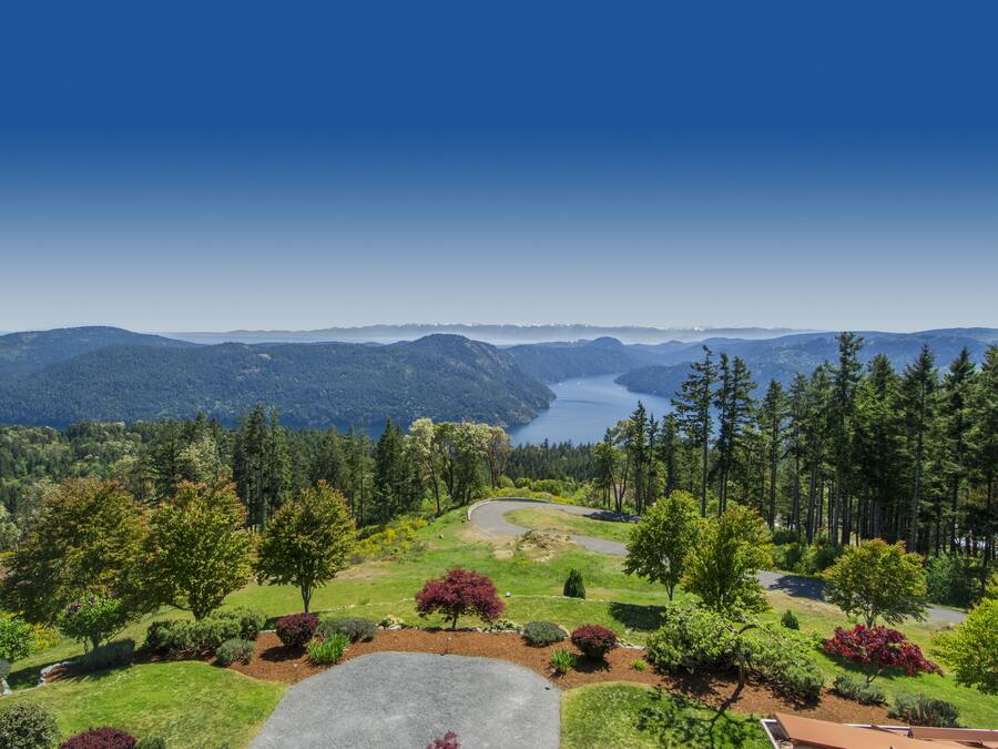 A scenic view of a mountainous landscape with a winding road, lush greenery, and a lake in the distance.