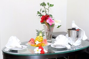 Uma mesa de vidro com um prato de frutas, um vaso com flores e duas taças de champanhe.